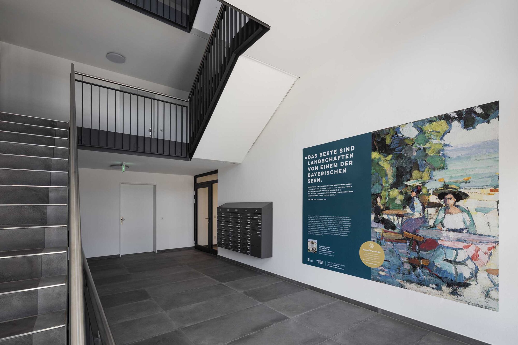 Moderner Eingangsbereich mit Treppe, Briefkästen und Kunstwerk an der Wand.