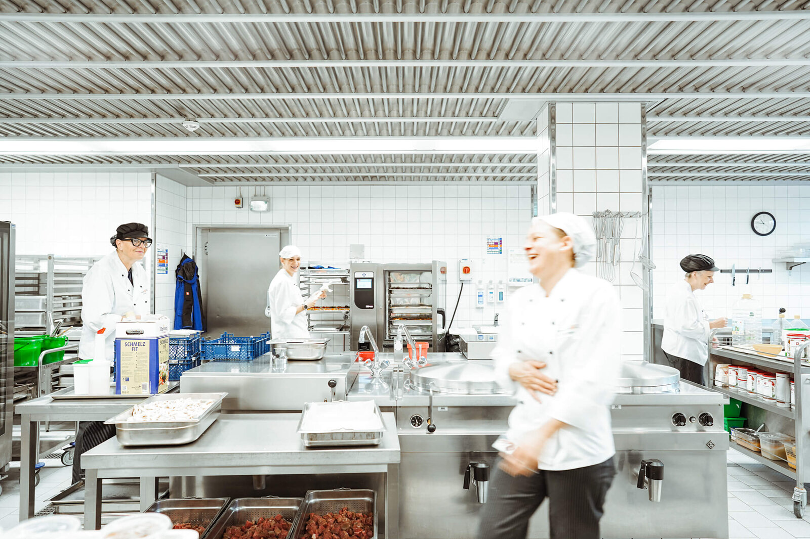 Mehrere Köchinnen und Köche arbeiten in einer Großküche an Edelstahl-Arbeitsflächen und Geräten in der Campusküche Bielefeld.