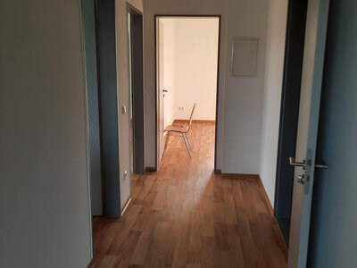 Heller Flur mit Holzfußboden, Türen zu Zimmern und einem Stuhl im Hintergrund.