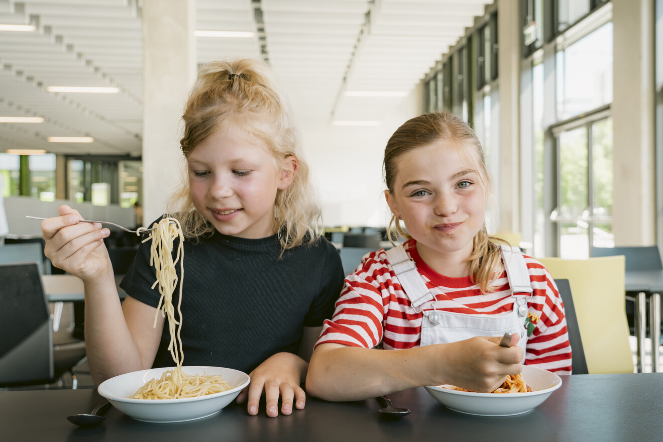 Zwei Kinder essen fröhlich Spaghetti.