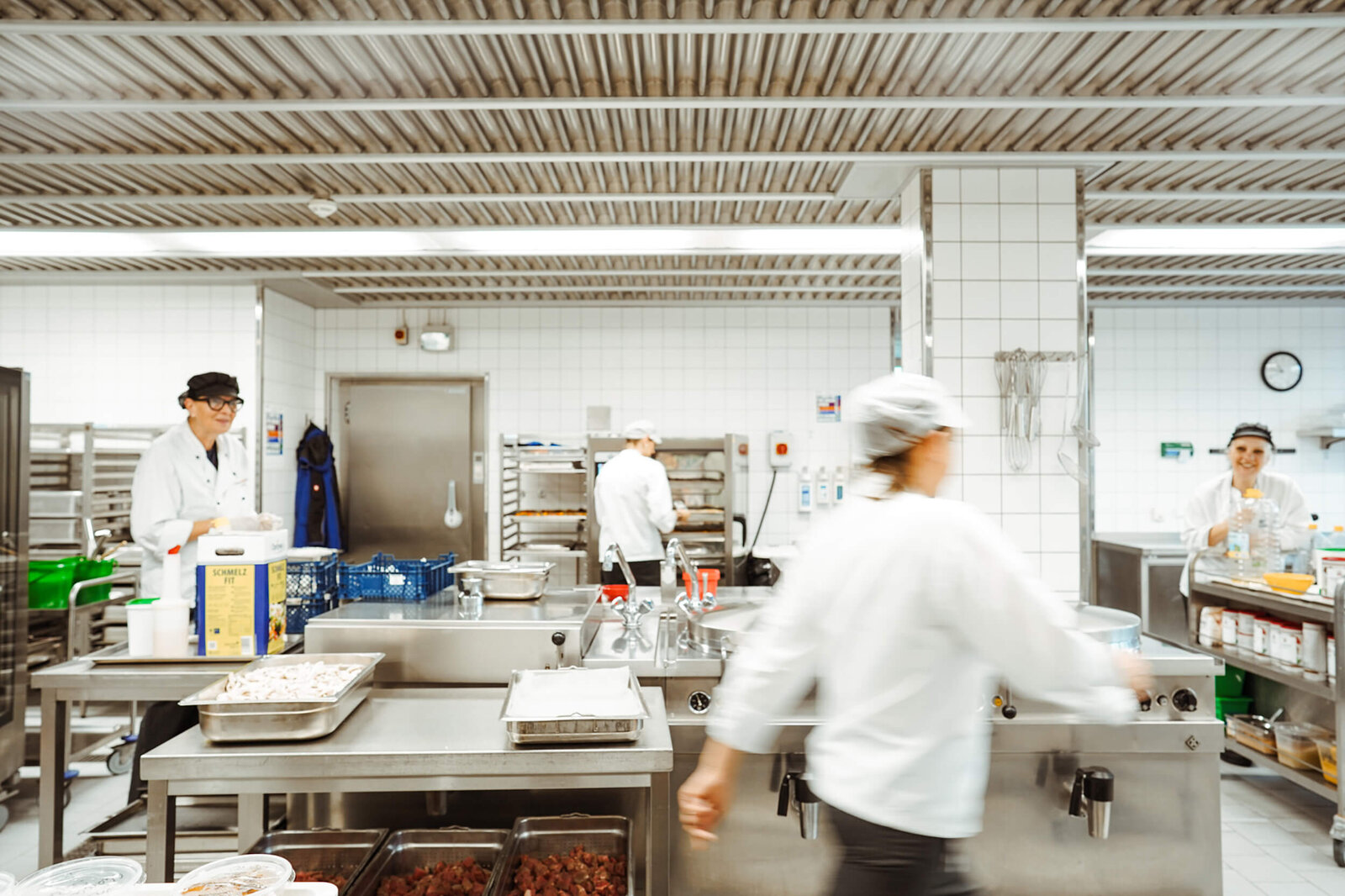 Mehrere Köchinnen und Köche arbeiten in einer Großküche an Edelstahl-Arbeitsflächen und Geräten in der Campusküche Bielefeld.