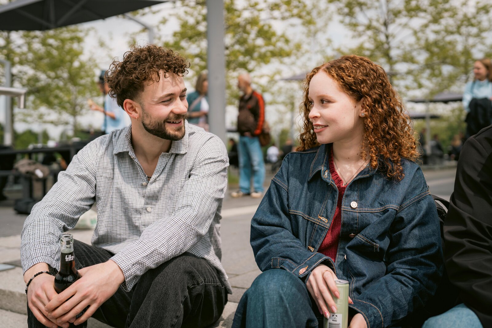 Ein junger Mann mit Flasche in der Hand unterhält sich mit einer jungen Frau im Sitzen.