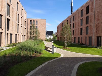 Blick auf moderne, rote Ziegelgebäude mit gepflegtem Garten und Rundweg zwischen den Gebäuden.