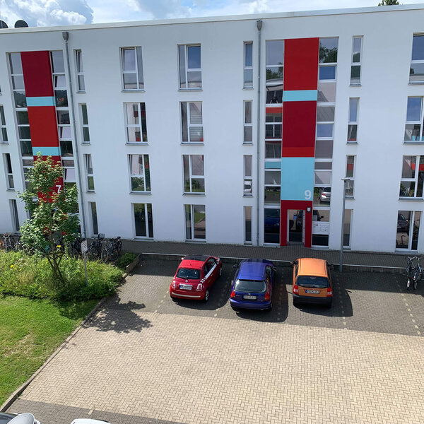 Fassade des Gebäudes Gutenbergstraße 1/13 mit bunten Akzenten und parkenden Autos.