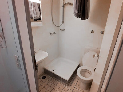 Kompakte Dusche mit WC, Waschbecken und Duschvorhang in minimalistischen Design.