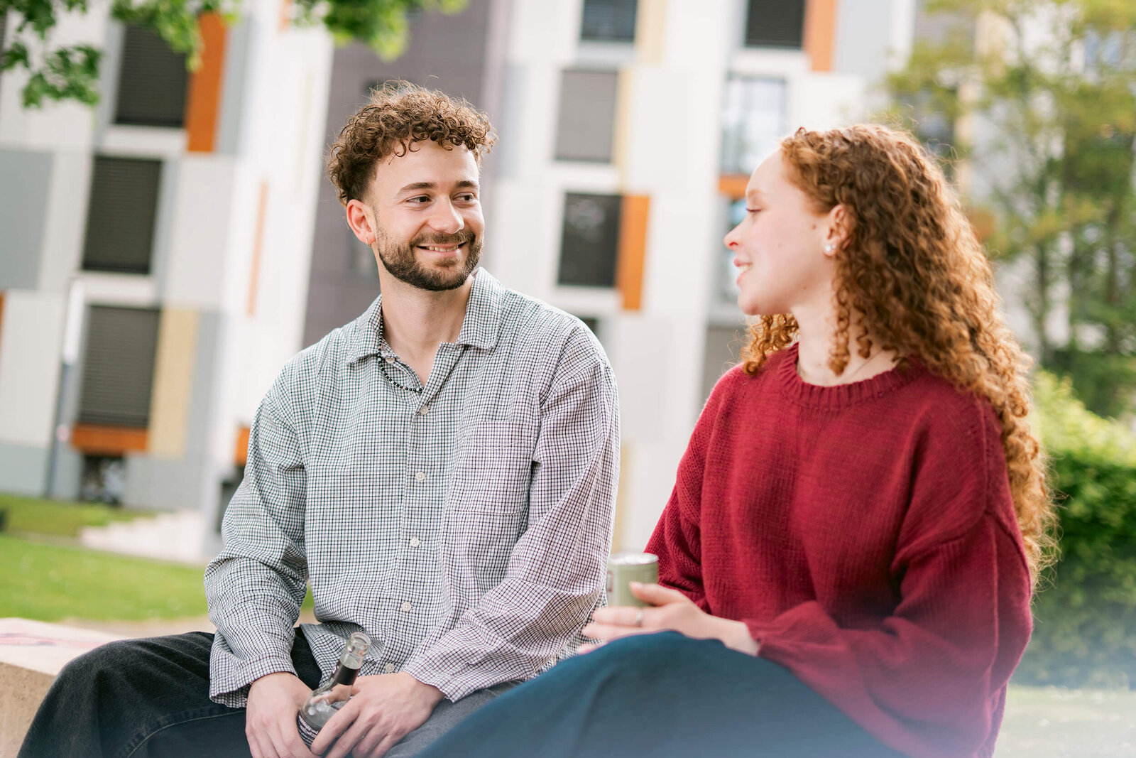 Zwei Personen sitzen auf einer Bank im Freien vor einem Gebäude des Studierendenwerks Bielefeld und unterhalten sich.