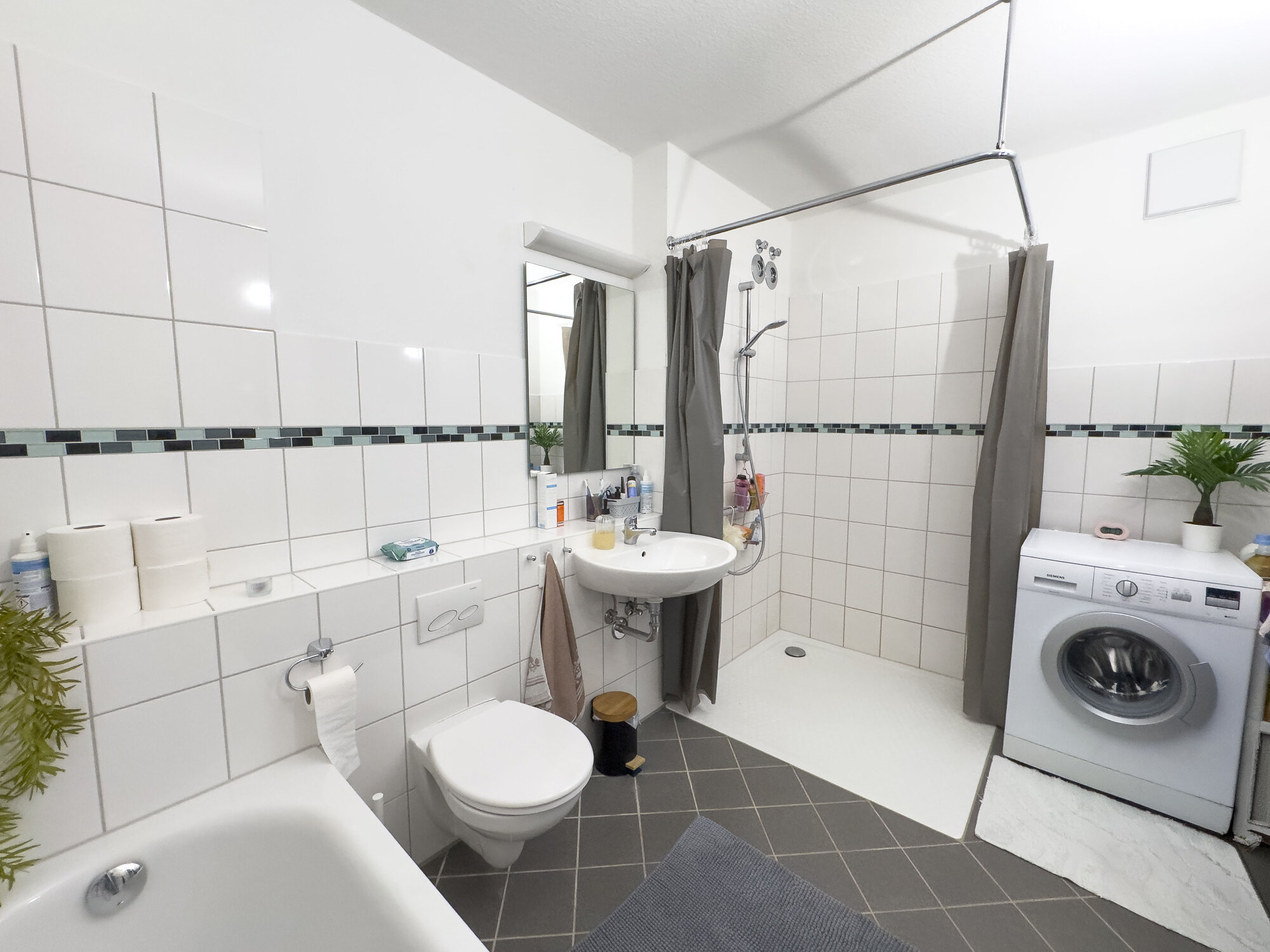 Badezimmer mit bodentiefer Dusche, Badewanne, Platz für Waschmaschine und Toilette