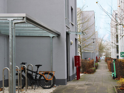 Fahrradständer mit einem schwarzen E-Bike und orangefarbener Rahmen bei einem modernen Gebäude.