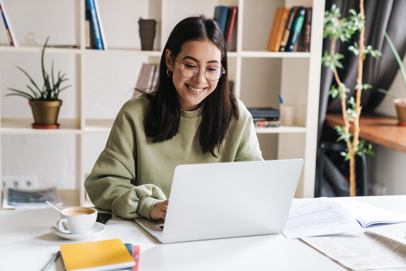 Junge Frau mit grünem Pullover sitzt lächelnd am Laptop.