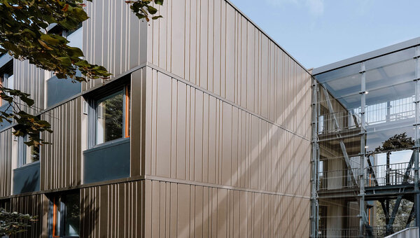 Moderne Gebäudefassade des Studierendenwerks Bielefeld mit vertikalen Metallpaneelen und mehreren Fenstern, daneben ein Treppenhaus mit offenen Gitterstrukturen.