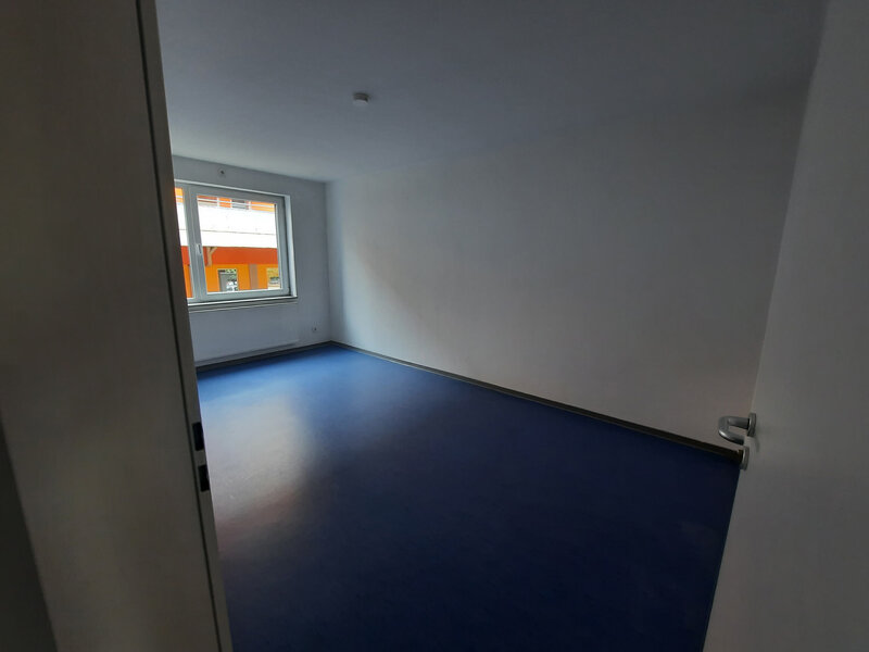 Helles Zimmer in einer 2er-WG mit blauem Boden und Fenster für natürliche Beleuchtung.