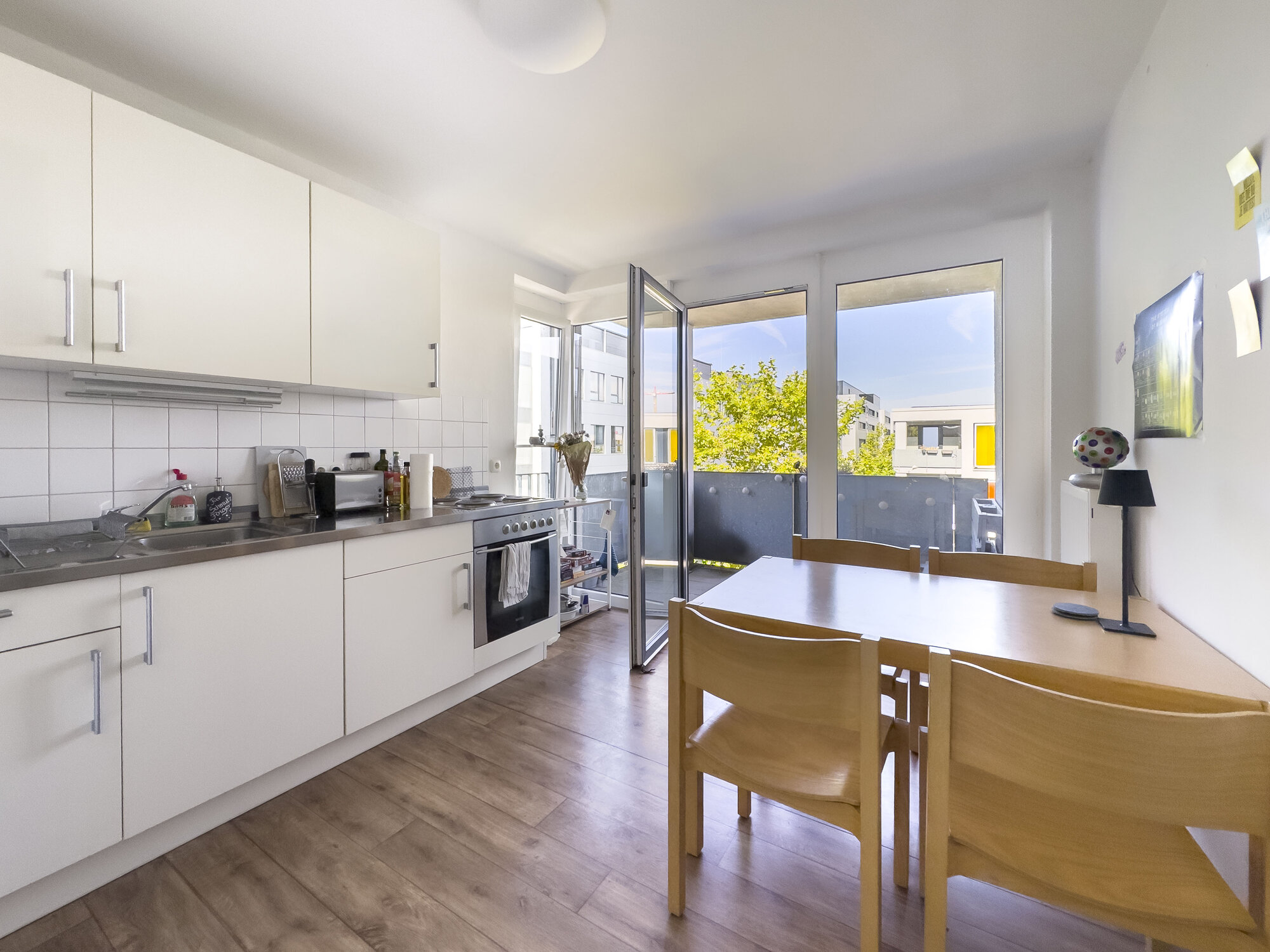 Helle WG-Küche mit großem Tisch und vier Stühlen mit Zugang zum Balkon