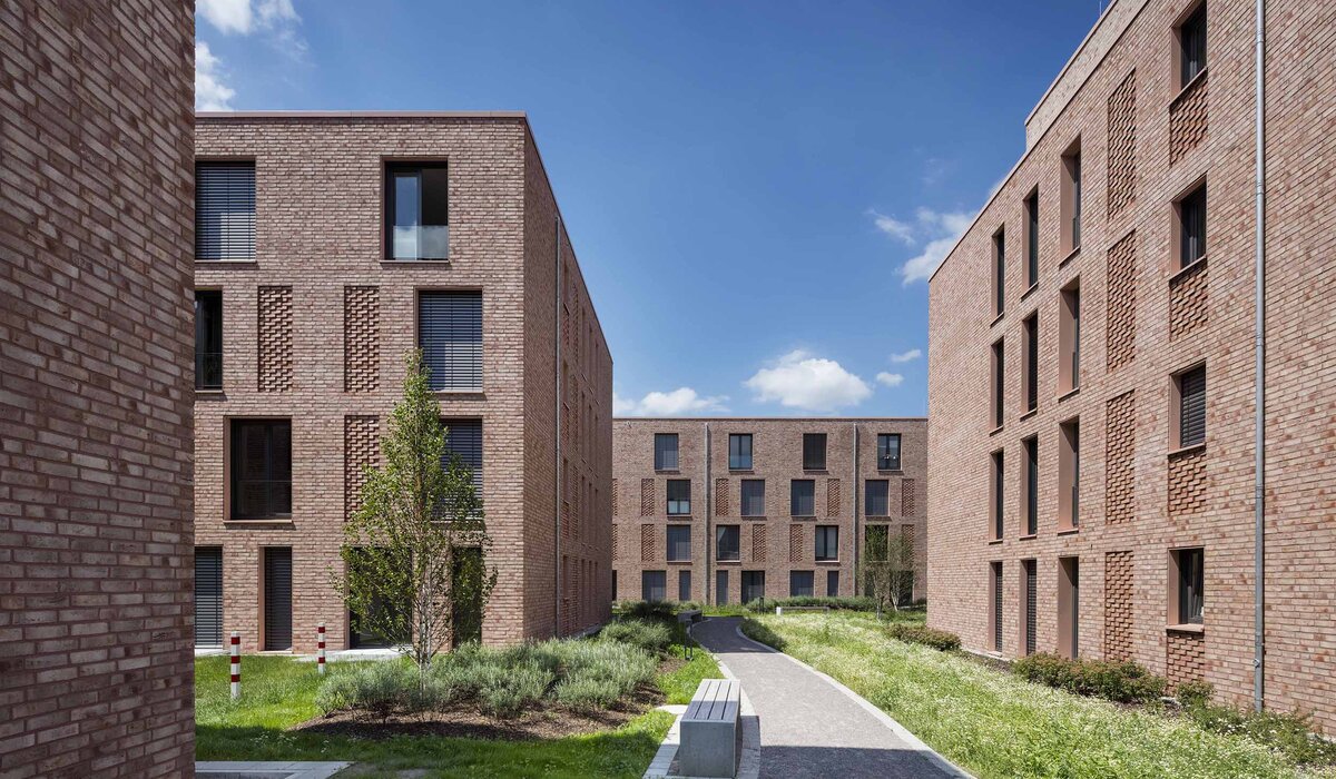 Moderne Wohnanlage "Stennerstr. 19, 21, 21a–c / Storchsbrede 23, 25" mit roten Ziegeln, begrünten Flächen und Fußweg zwischen den Gebäuden.