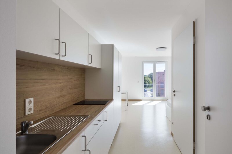 Moderne Küche mit Holzarbeitsplatte, Edelstahlspüle und Kochfeld, große Fenster erschaffen hellen Raum.