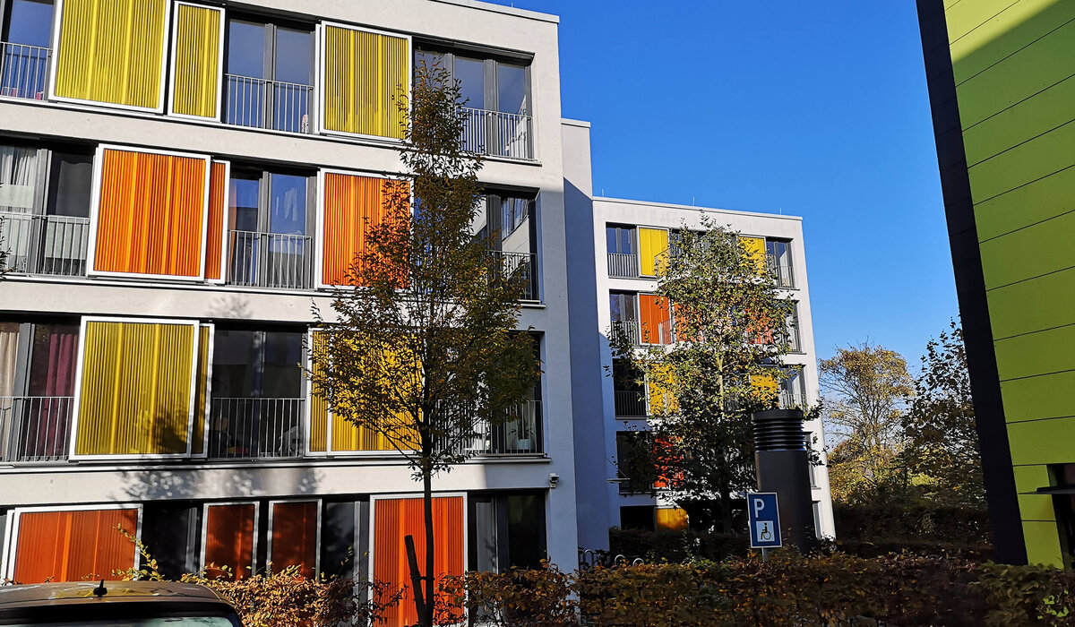 Moderne Wohnanlage "Morgenbreede 6+10+14" mit farbigen Fenstern in Gelb und Orange unter klarem blauen Himmel.