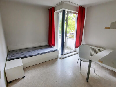 Helle Studiozimmer mit rotem Vorhang, Einzelbett, Tisch und Stuhl sowie Zugang zum Balkon.