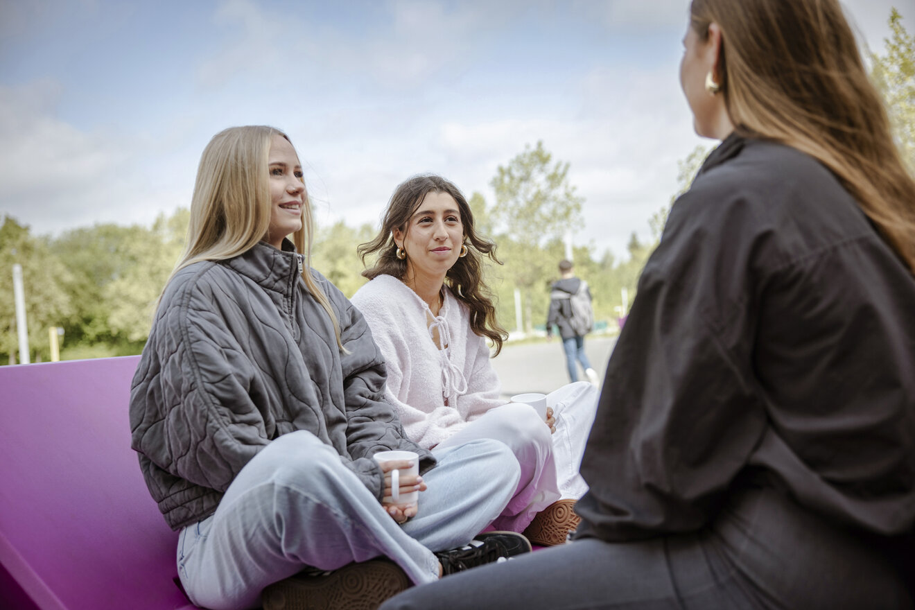 Drei junge Frauen in lässiger Kleidung sitzen im Freien und unterhalten sich.