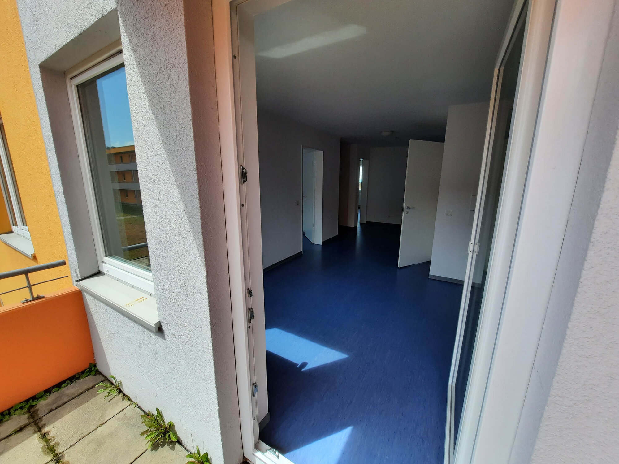Blick vom Balkon in eine Wohnung mit blauen Bodenfliesen und hellen Wänden.