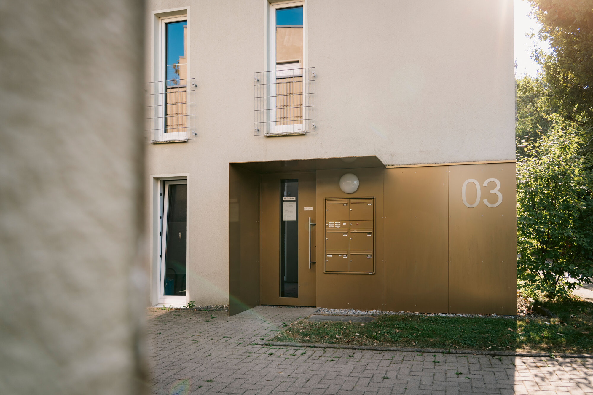Moderne Fassade mit großen Fenstern und einem goldenen Eingangsbereich, umgeben von Pflastersteinen.