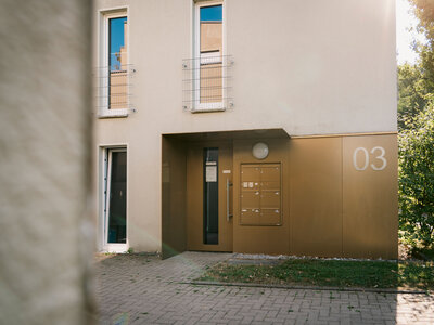 Moderne Fassade mit großen Fenstern und einem goldenen Eingangsbereich, umgeben von Pflastersteinen.