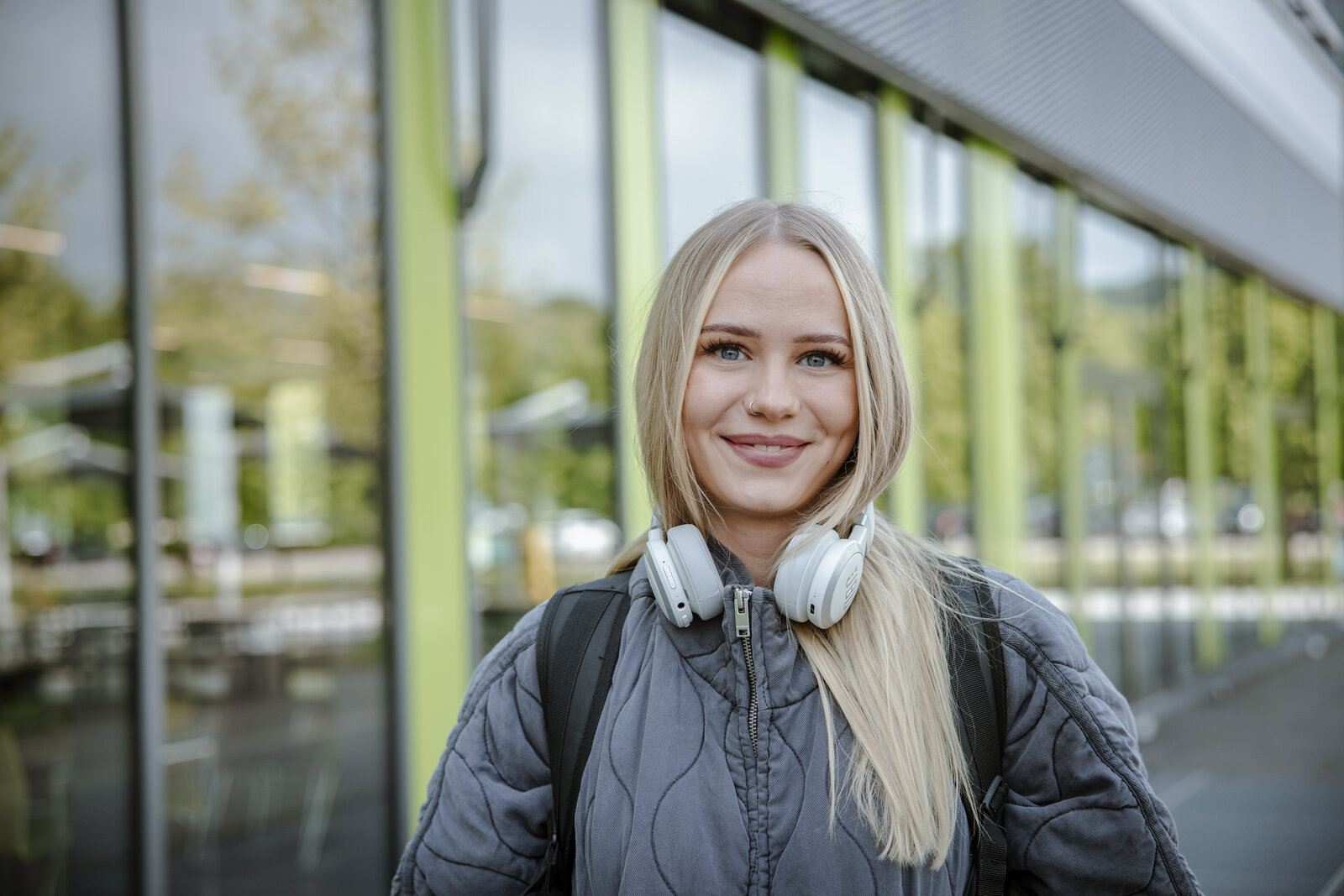 Studentin mit Kopfhörern lehnt an einer Fensterscheibe.