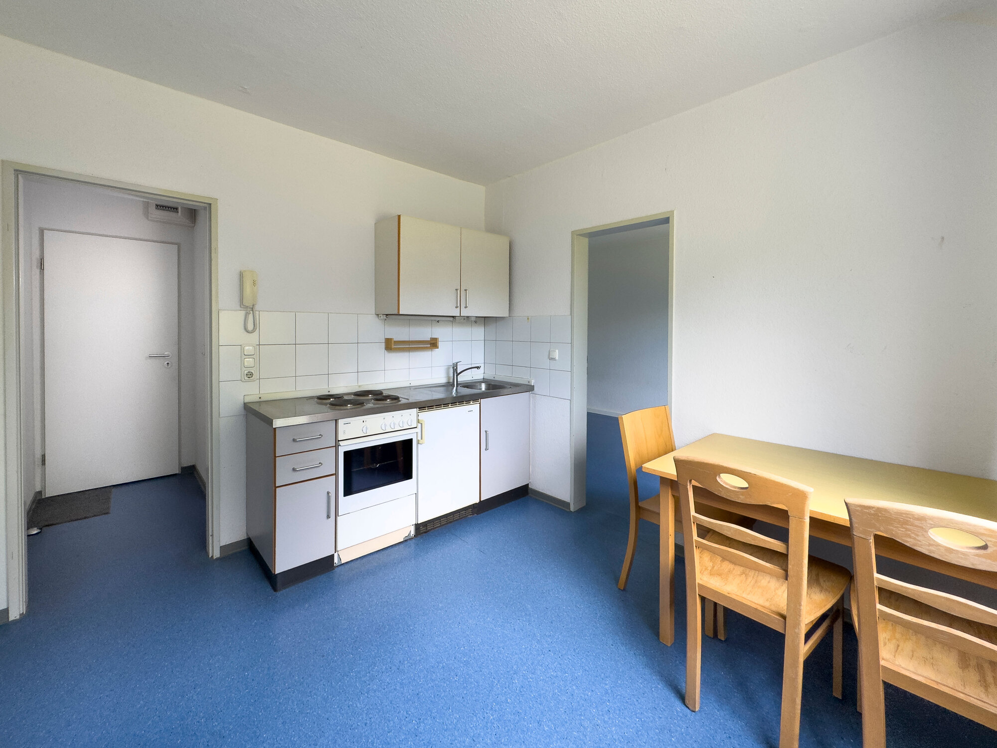 Wohnküche mit Herd, Tisch und Stühlen und Abzweig zum Flur und zum WG-Zimmer