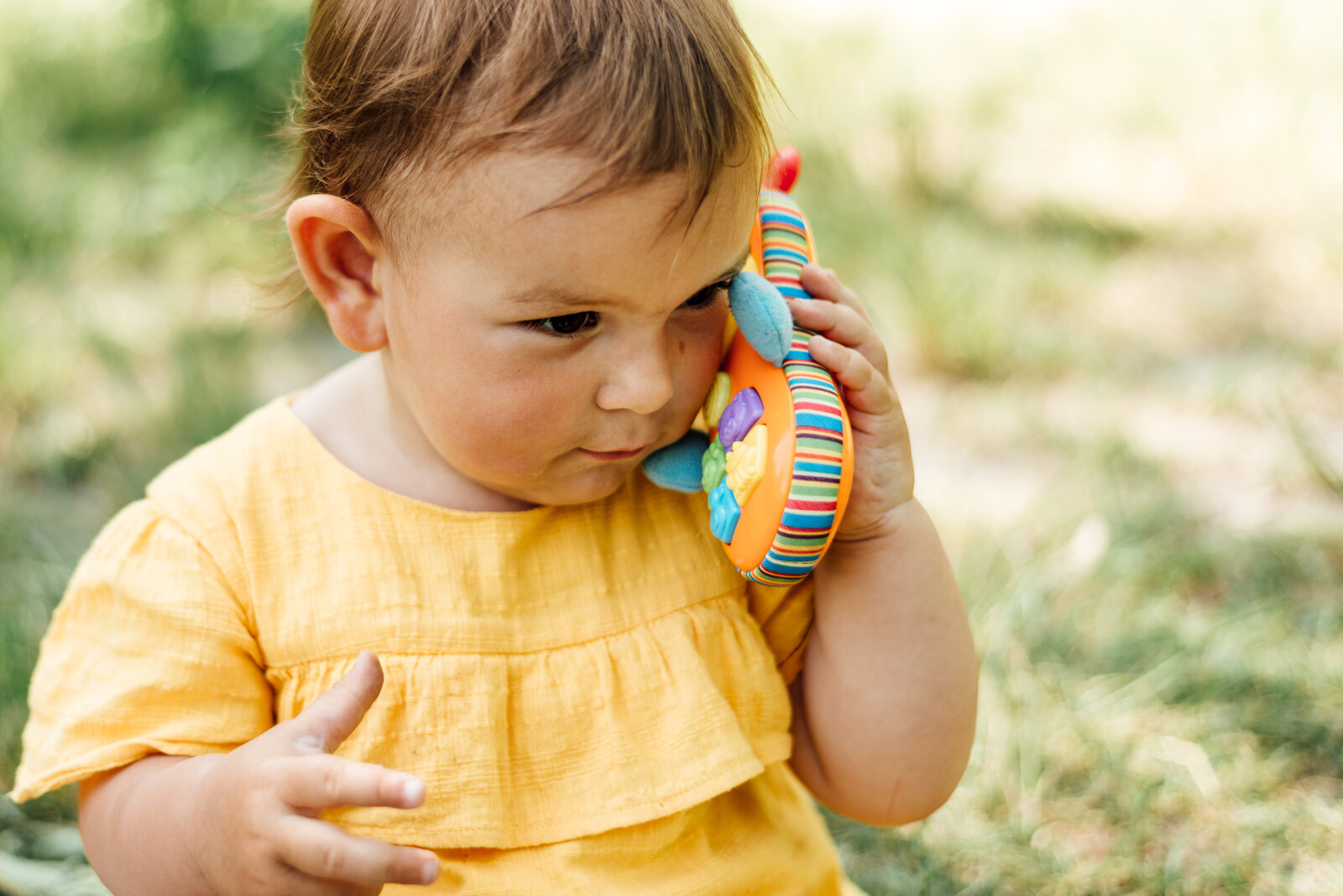 Kleines Kind sitzt auf Rasen mit Spielzeugtelefon in der Hand.