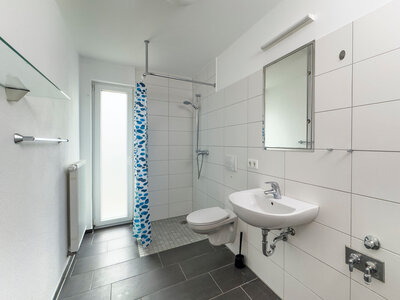 Helles Badezimmer mit bodentiefer Dusche, gefliestem Boden und Wänden und Spiegel.