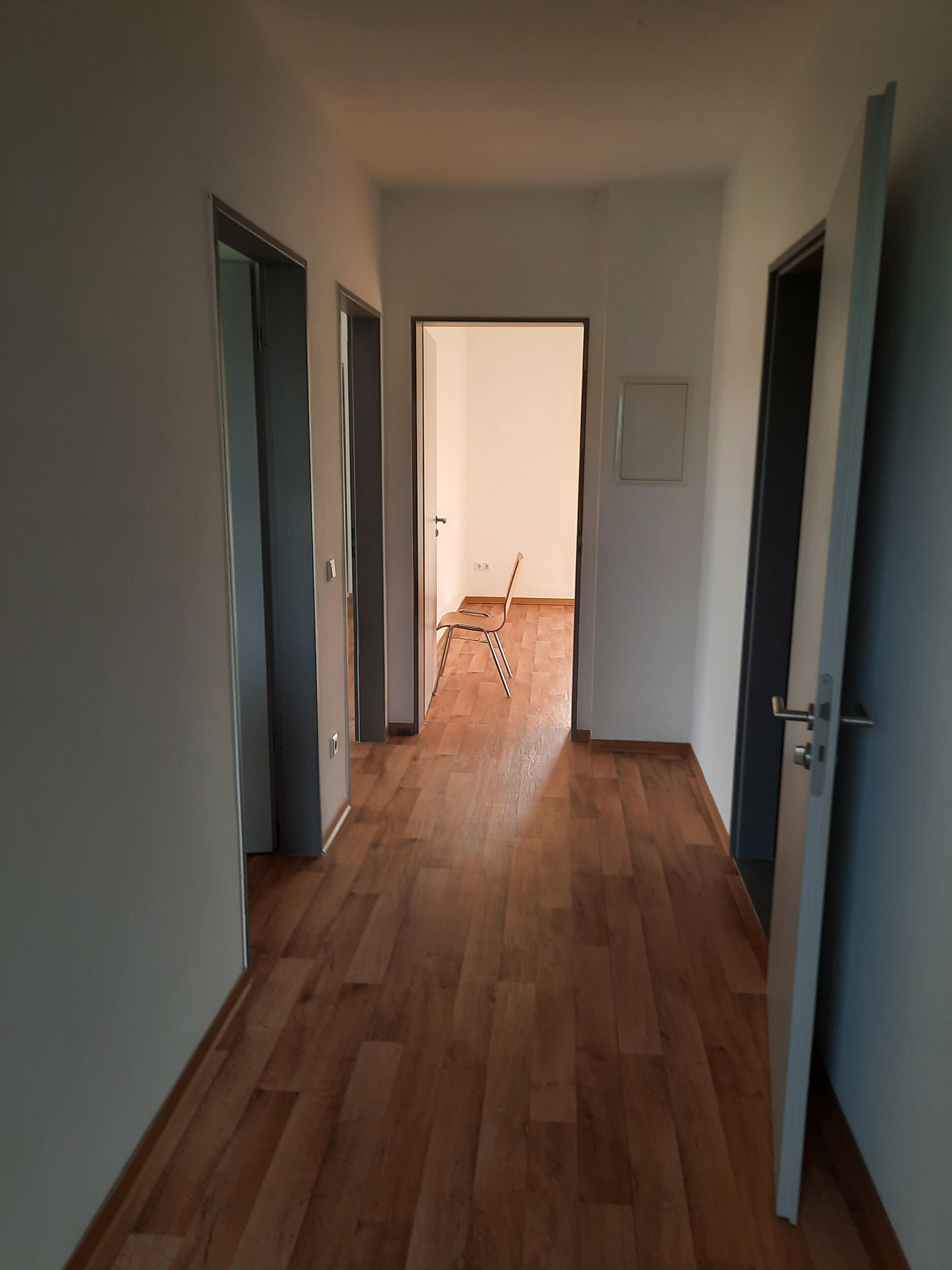 Heller Flur mit Holzfußboden, Türen zu Zimmern und einem Stuhl im Hintergrund.