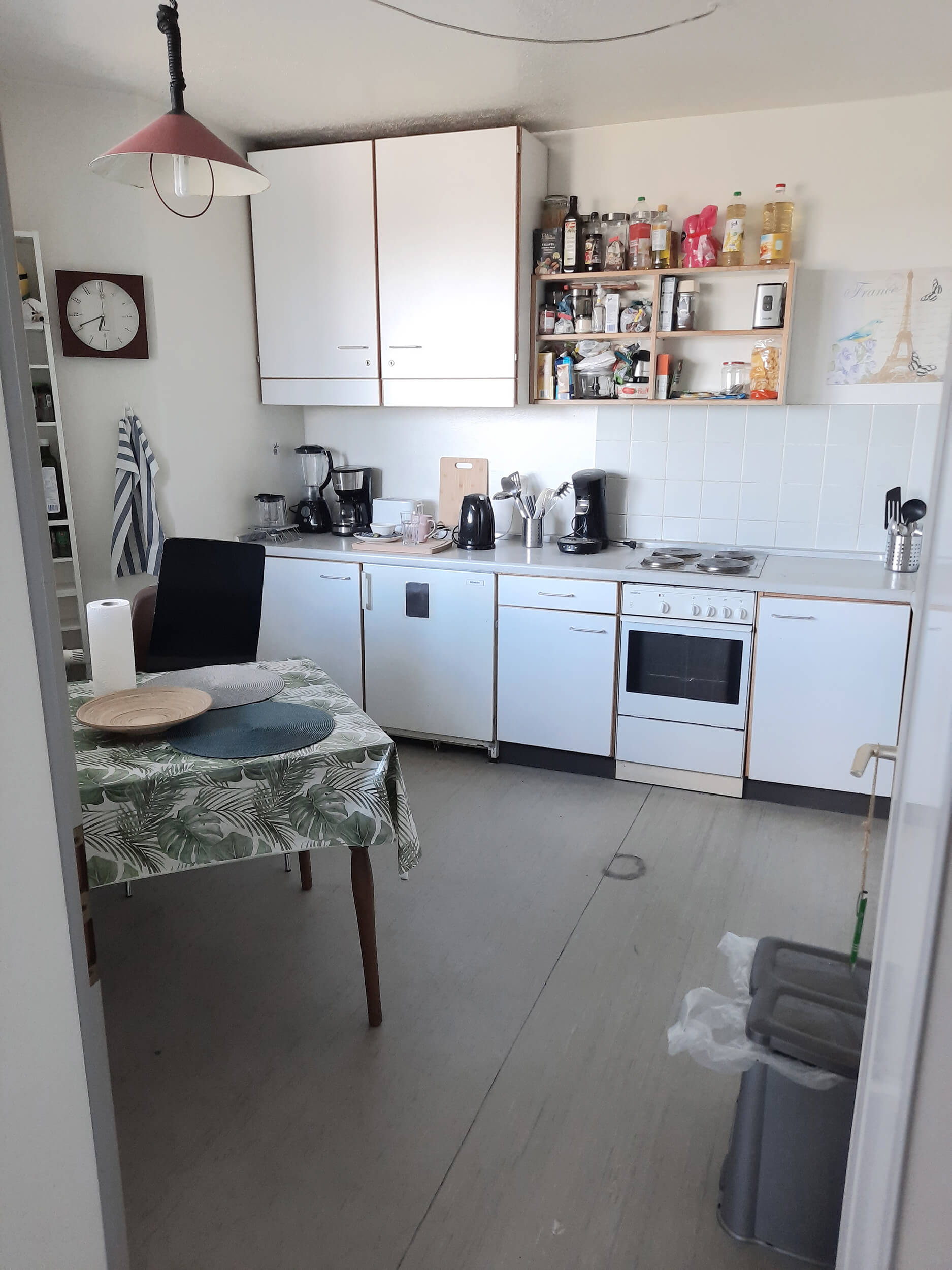 Helle Küche mit weißen Schränken, Kaffeeautomaten, Gasherd und Esstisch mit grüner Tischdecke.